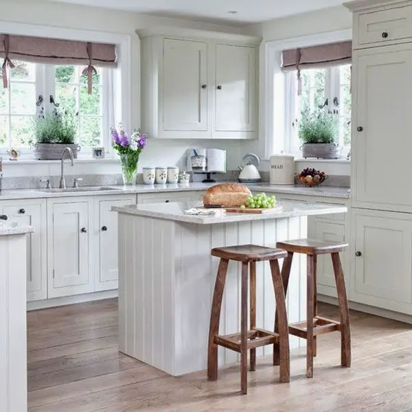 Love this small white cottage farmhouse kitchen.  The gray countertops give a little offset to all the white and the curtain valances give a little pop of color.  Good use of a small island in this tiny kitchen.